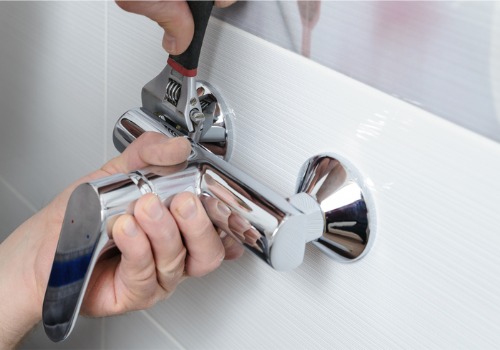 A plumber adjusting a bathtub's faucet, part of bathroom plumbing