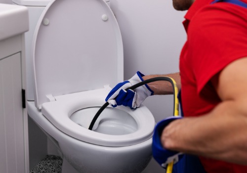 A residential plumber using a pipe snake to unclog a toilet